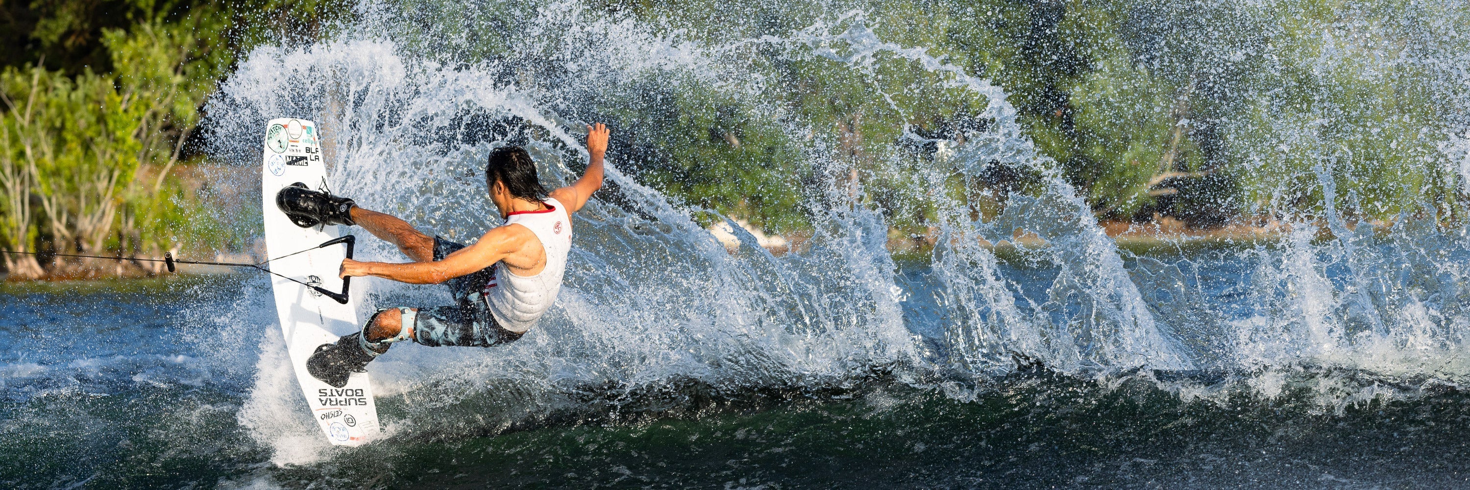 A wakeboarder carves through the water, creating a dramatic spray while holding a handle attached to a tow rope.