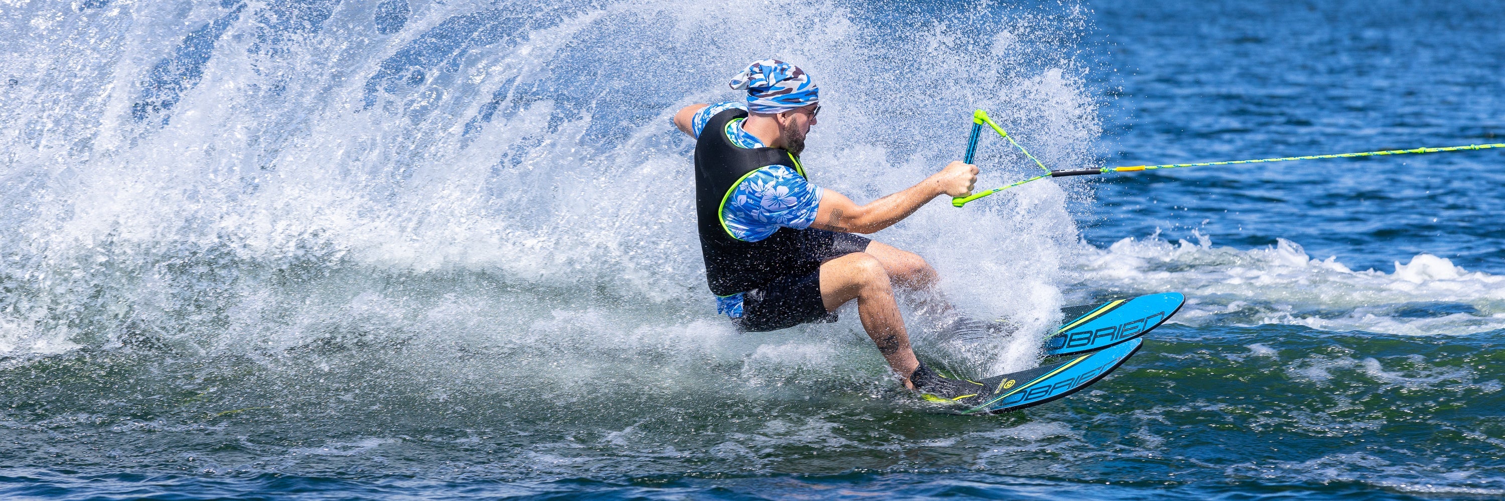 A waterskier in a black vest kicks up water while gripping a bright yellow tow rope.