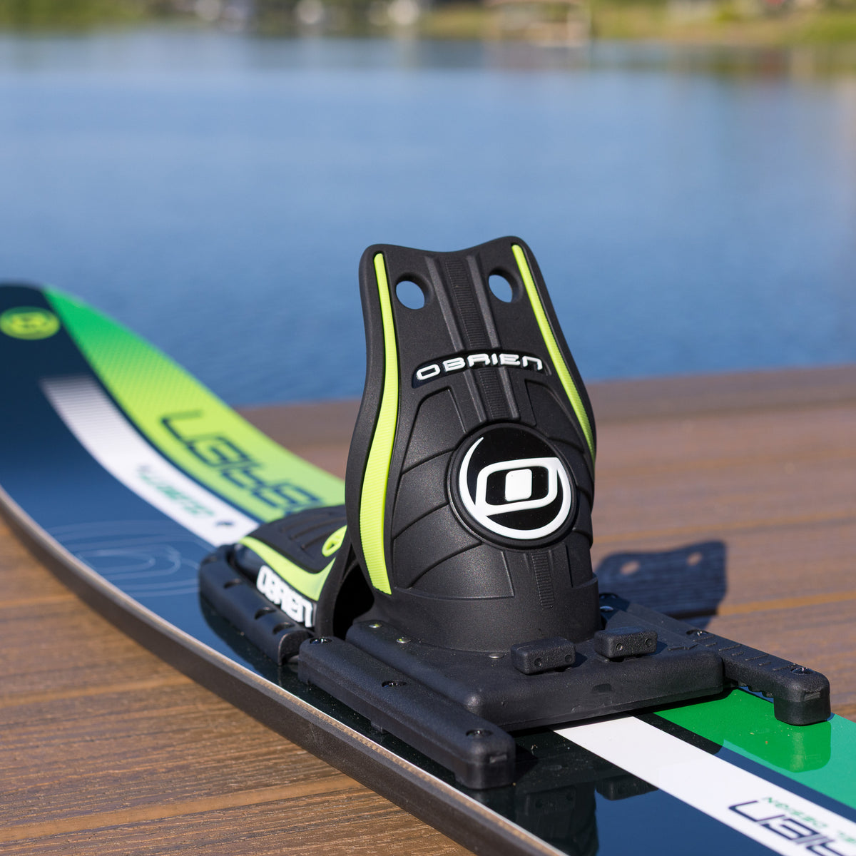 Black and green water ski on a wooden dock with water in the background