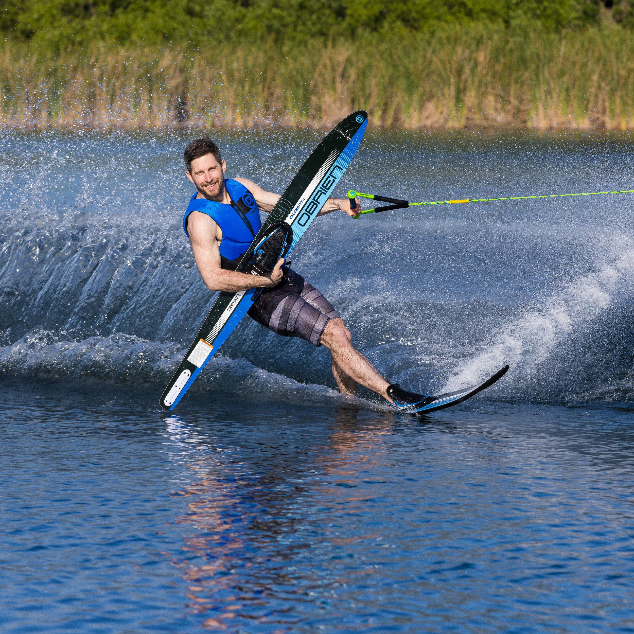 Man holding a water ski and water skiing on a lake with greenery in the background