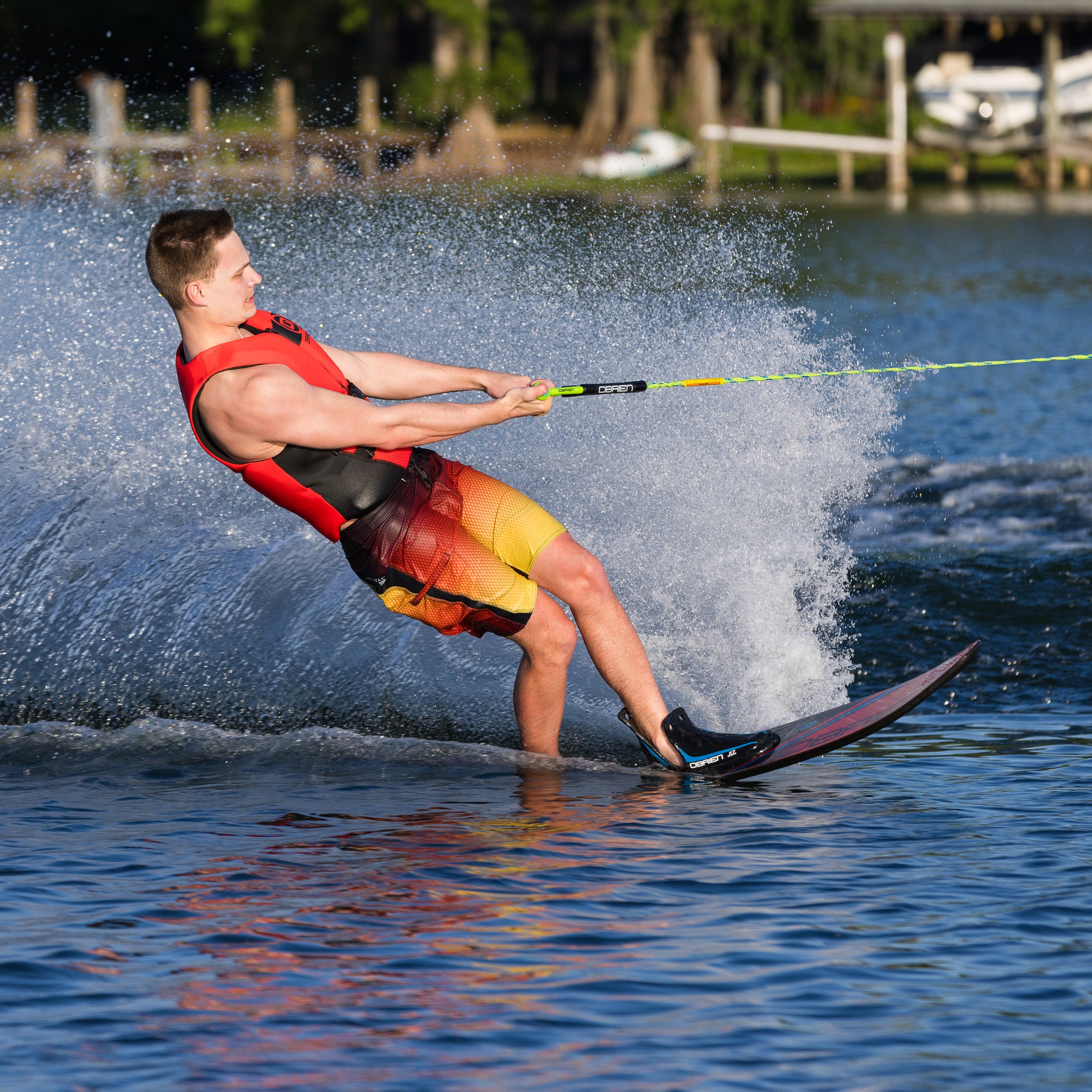 Person water skiing on a lake with a red life jacket and yellow shorts.